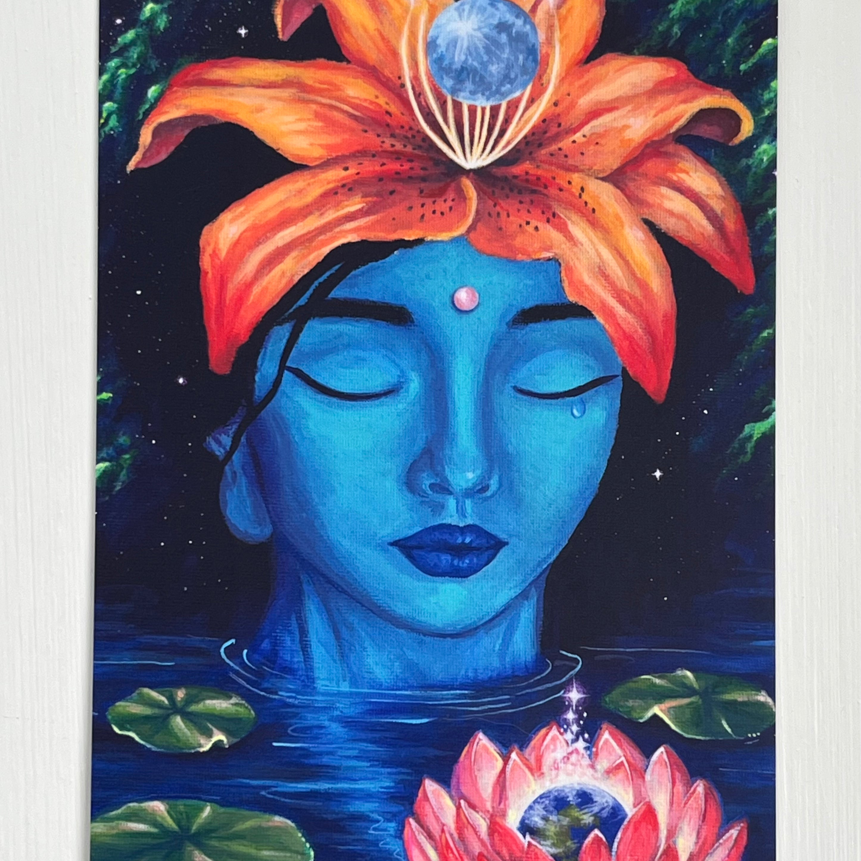 A postcard depicting a blue-skinned goddess Kuan Yin wearing a tiger lily headdress. containing the moon. A single tear escapes from her eye. She rests peacefully with her eyes closed in a body of water, surrounded by lilypads and a glowing lotus containing planet Earth.