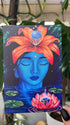 A hand holds up a postcard depicting a blue-skinned goddess Kuan Yin wearing a tiger lily headdress. containing the moon. A single tear escapes from her eye. She rests peacefully with her eyes closed in a body of water, surrounded by lilypads and a glowing lotus containing planet Earth.