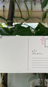 A hand holds up a postcard and shows off the back of the card, which features ample blank space on the left for message-writing, and on the right, a place for a stamp and a section for the address.