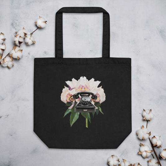 A black tote bag showcasing a design of a black rotary telephone set against a background of large, blooming white peonies with green leaves.