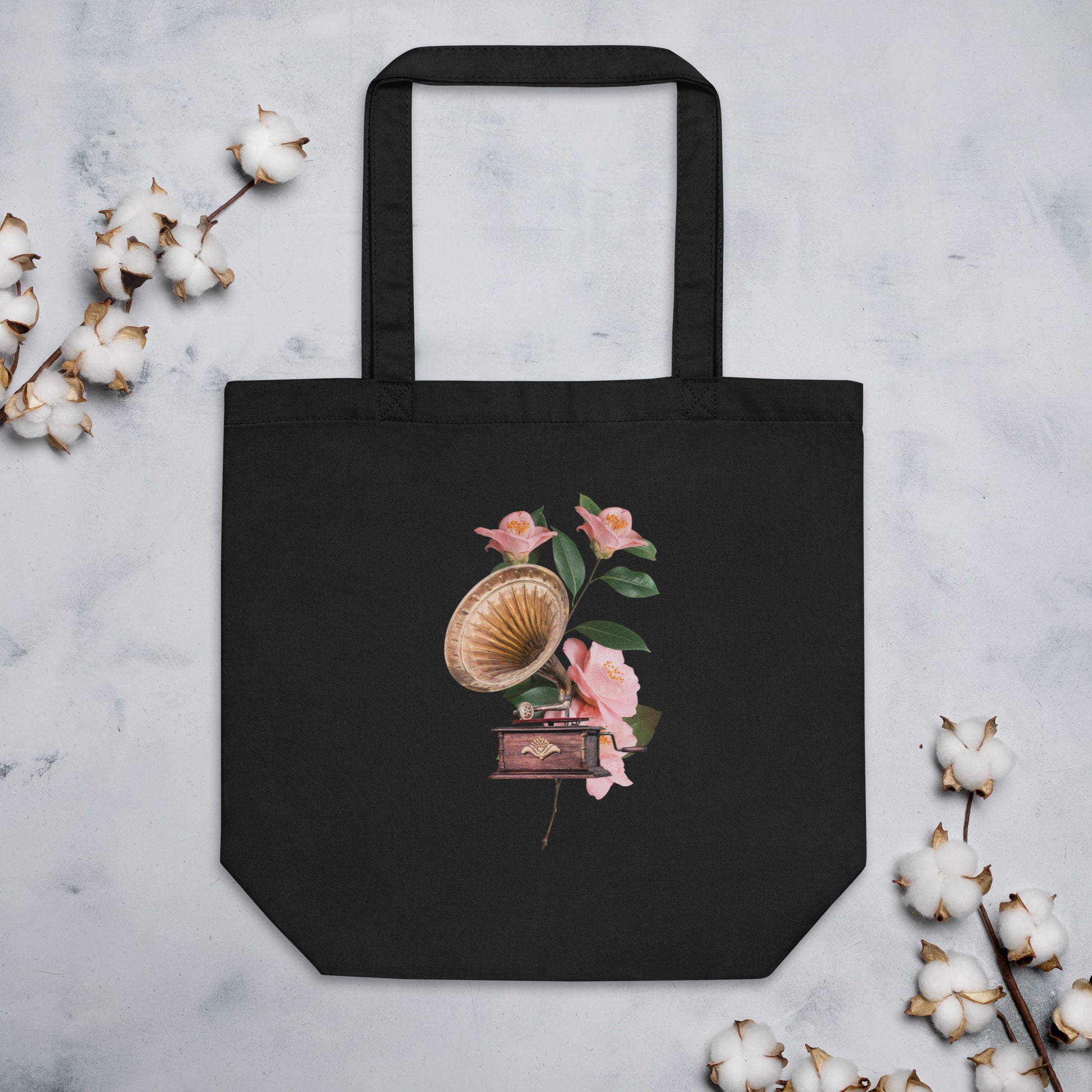 A black tote bag featuring a design of a vintage gramophone with a wooden base and a brass horn, surrounded by delicate pink flowers with green leaves.