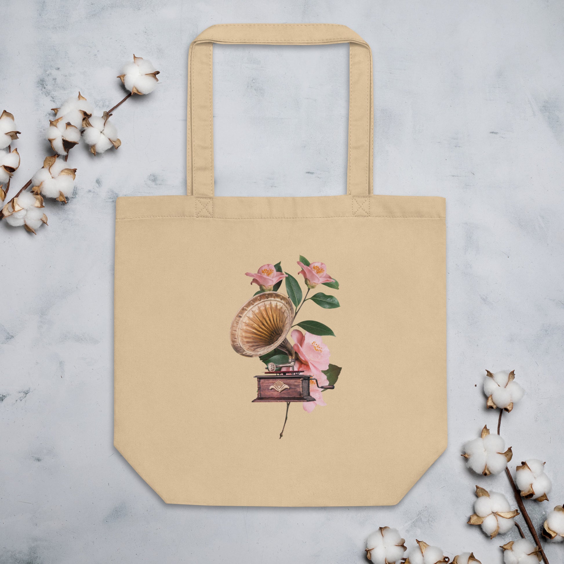 A tan tote bag featuring a design of a vintage gramophone with a wooden base and a brass horn, surrounded by delicate pink flowers with green leaves.