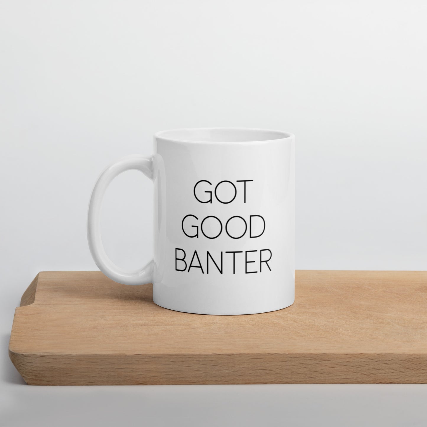 A glossy white ceramic mug with thin, all-caps black sans serif font that reads 'GOT GOOD BANTER', positioned on a wooden cutting board against a neutral background.