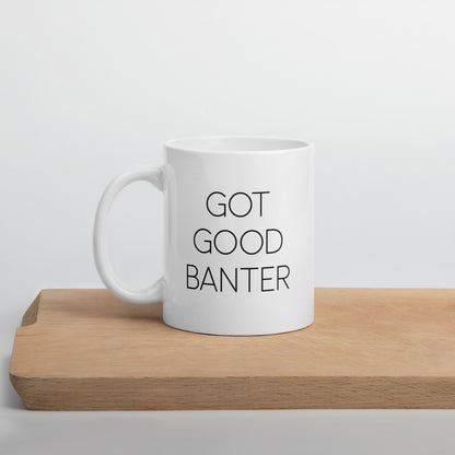 A glossy white ceramic mug with thin, all-caps black sans serif font that reads 'GOT GOOD BANTER', positioned on a wooden cutting board against a neutral background.