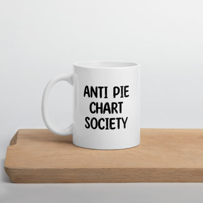 A white ceramic mug with all-uppercase black bubble text that reads 'ANTI PIE CHART SOCIETY', positioned on a wooden cutting board against a neutral background.