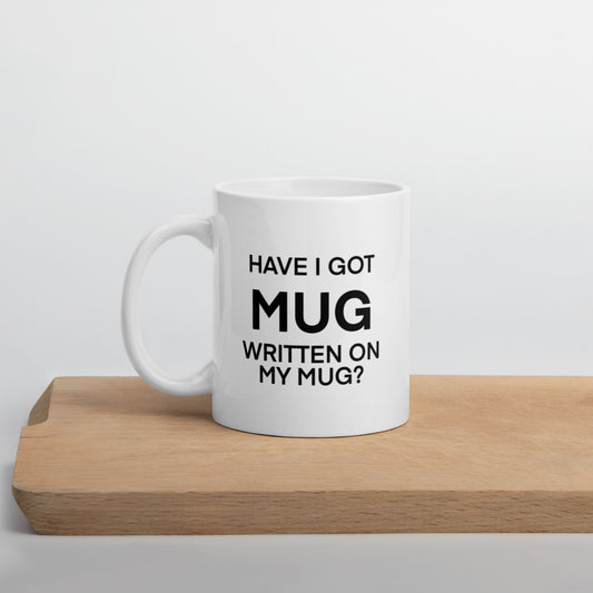 A glossy white ceramic mug with black bolded sans serif text that reads 'HAVE I GOT MUG WRITTEN ON MY MUG?', where the first 'MUG' is in bigger font size, positioned on a wooden cutting board against a neutral background.