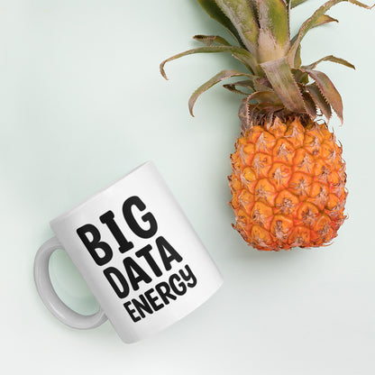 A glossy white ceramic mug with bolded black bubble text that reads 'BIG DATA ENERGY', lies on its side next to a pineapple against a pastel light mint background.