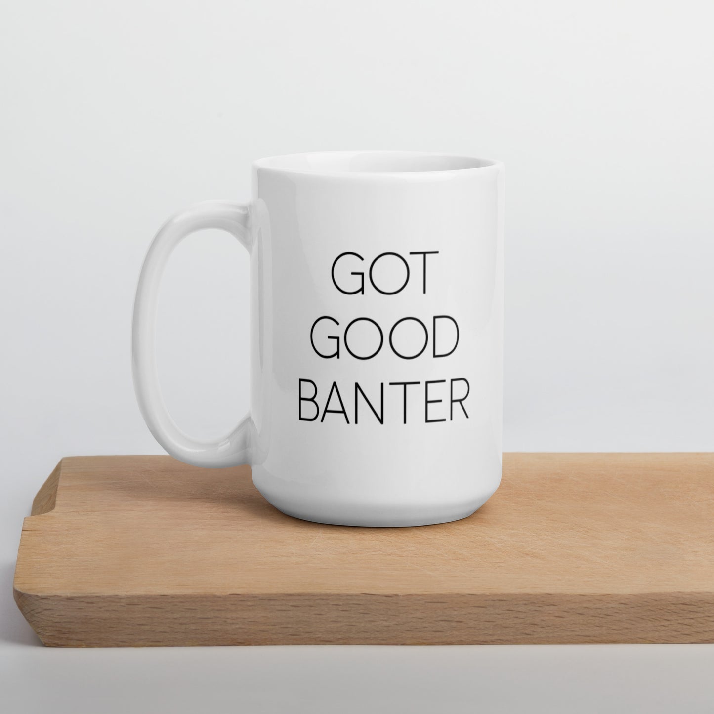 A glossy white ceramic mug with thin, all-caps black sans serif font that reads 'GOT GOOD BANTER', positioned on a wooden cutting board against a neutral background.