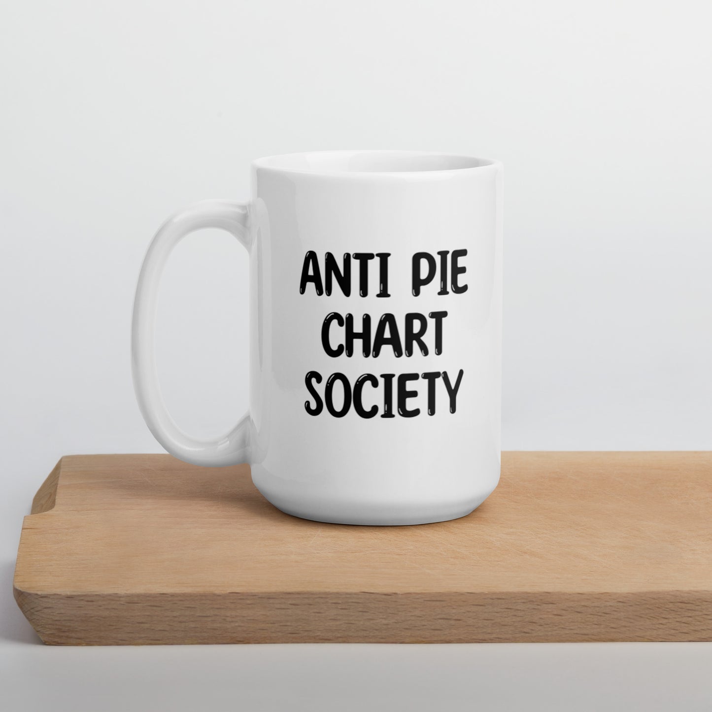 A white ceramic mug with all-uppercase black bubble text that reads 'ANTI PIE CHART SOCIETY', positioned on a wooden cutting board against a neutral background.